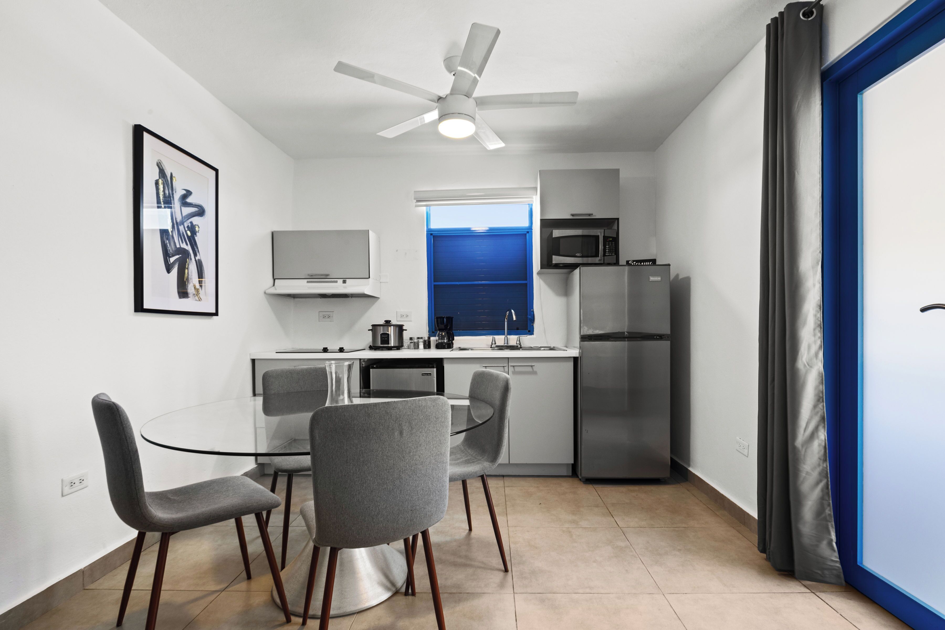 Cocina moderna con comedor, paredes blancas, ventilador de techo y vistas a través de una ventana.