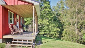 A red cabin with a wooden deck, outdoor seating, and a view of the surrounding forest. - Picturesque Cabin set on 150-acre farm, 5-minute drive to Chautauqua Institute (Mayville)