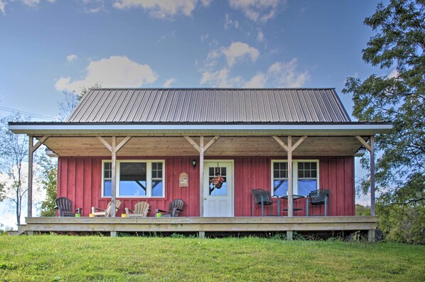 A red wooden building with a porch, two windows, and a door.
