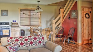 A cozy living room with a sofa, wooden dining table, and chairs. A kitchen area with a stove and cabinets is visible in the background. - Picturesque Cabin set on 150-acre farm, 5-minute drive to Chautauqua Institute (Mayville)