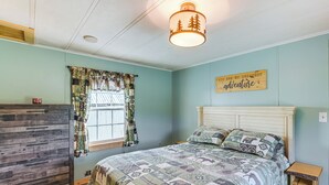 Een slaapkamer met een bed, een dressoir, een raam met gordijnen met een patroon, en een bord aan de muur.