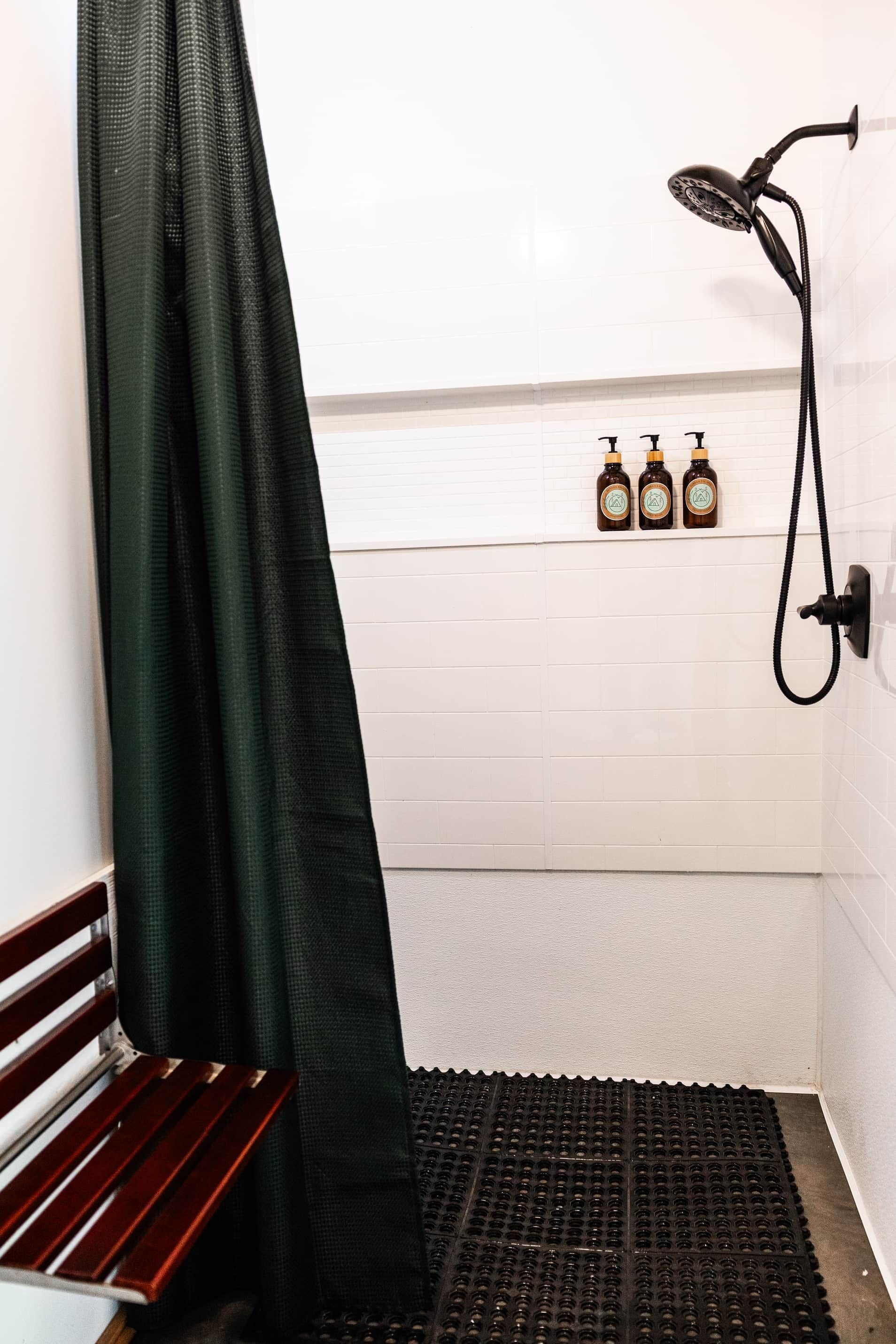 Ein Duschbereich mit Sitzbank, Duschkopf und drei Shampoo-Flaschen an der Wand.