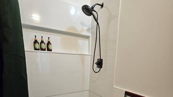 A small, enclosed shower area with white tiled walls, a handheld showerhead, and a bench.