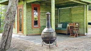 A rustic cabin with a chimney, a covered porch, and a seating area with a green couch and wooden chairs. - Sunken Escapes Bear Cub Cabin #9 (Sunken Lake)