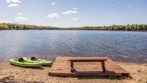 A wooden dock with a bench and two kayaks by a calm lake.