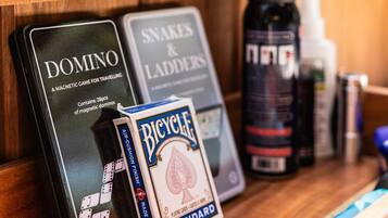 A wooden shelf with a magnetic game called Domino, a game called Snakes & Ladders, a Bicycle playing card deck, and a spray bottle.