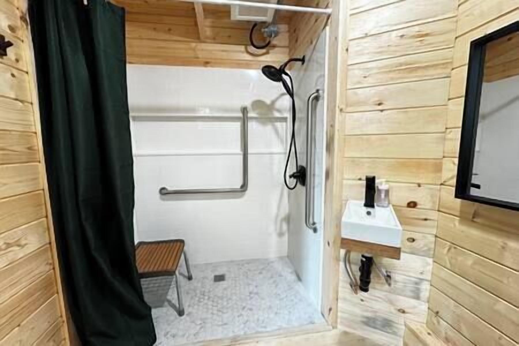 A wooden cabin bathroom with a shower, a small sink, and a wooden stool.