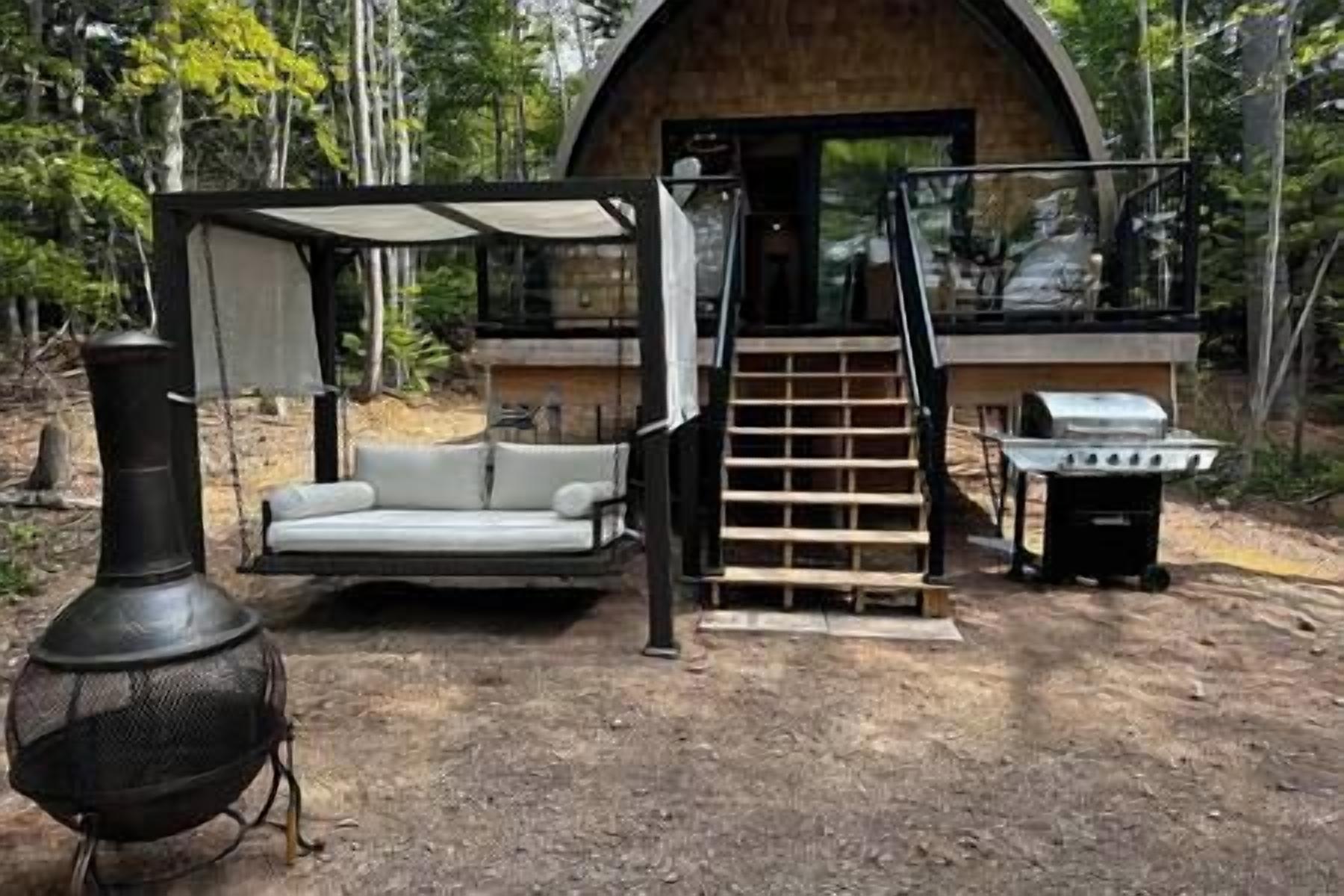A rustic cabin with a covered seating area, a grill, and a chimney.