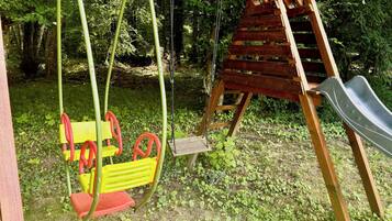 A wooden swing set with a slide, surrounded by greenery.