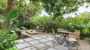 Un patio al aire libre con suelo de piedra, mobiliario de mimbre y abundante vegetación.