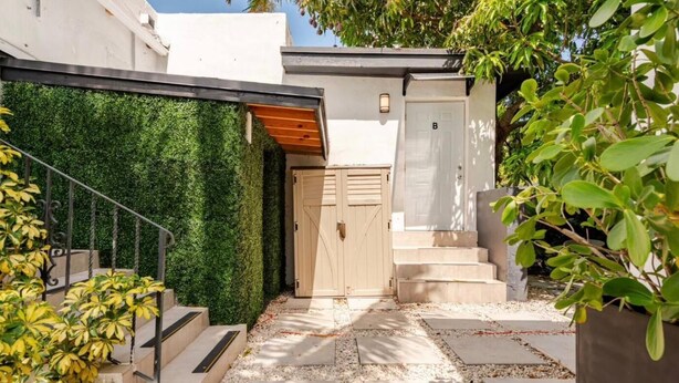 Una entrada exterior moderna con una escalera de madera, una pared verde y una puerta con la inscripción 'B'.