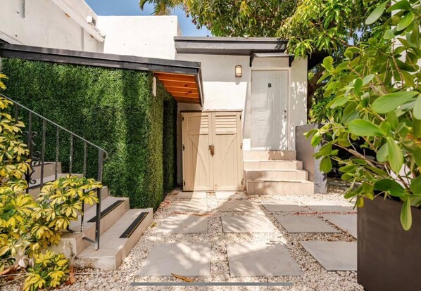 A modern outdoor entrance with a wooden staircase, a green wall, and a door marked 'B'.
