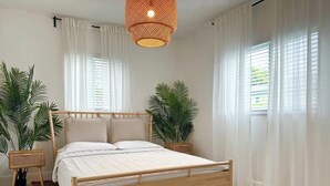 Un dormitorio con cama de madera, ropa de cama blanca, un tapete estampado y dos plantas en macetas.