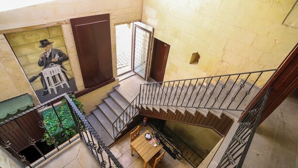Un interior de varios niveles con una escalera, una pequeña mesa con objetos y un mural en la pared.
