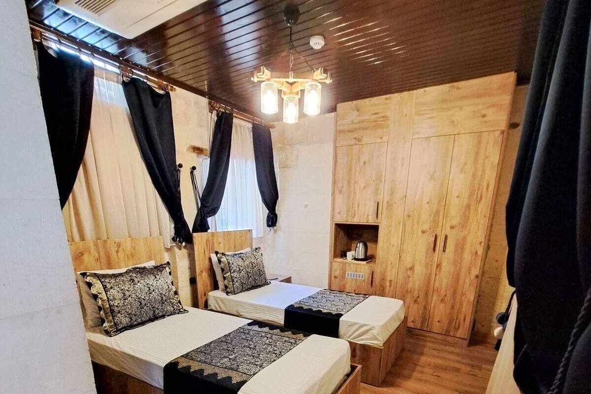 A wooden interior with two beds, a shelf with a kettle, and a ceiling vent.