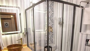 Un baño con tocador de madera, lavamanos sobre encimera, ducha con cerramiento de vidrio y un inodoro.