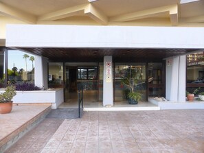 L’entrée d’un hôtel, avec un passage couvert, des plantes en pot et un panneau indiquant qu’il est interdit de fumer.