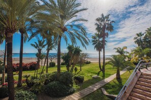 Un jardin en bord de mer, avec des palmiers, un sentier en bois et une vue sur la mer.