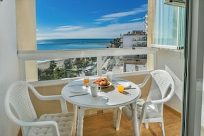 A balcony with a table set for breakfast, overlooking a beach and buildings.