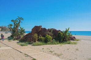 A sandy beach with a wooden boardwalk, palm trees, and large rock formations. - Lovely apartment 50m from the beach! (Fuengirola)