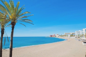 A beach with palm trees, a clear blue sky, and buildings in the background. - Great Apartment Amazing Seaview! 5 Pools, Pool bar (Benalmadena)