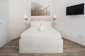 Une chambre moderne avec un lit blanc, un téléviseur fixé au mur et un tableau représentant un pont.