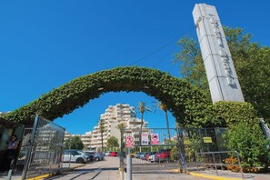 A gated entrance with a metal archway, a tall monument, and a multi-story building in the background. - Great Apartment Amazing Seaview! 5 Pools, Pool bar (Benalmadena)