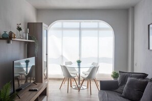 Una sala moderna con una mesa de comedor de vidrio, un sofá gris y un televisor sobre un mueble de madera.