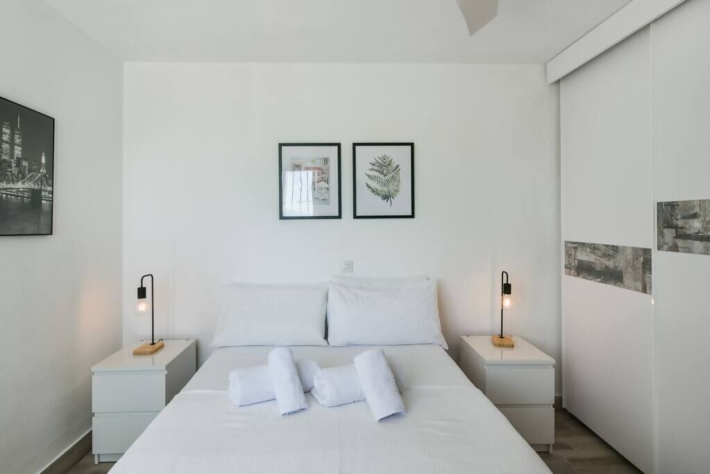 A modern hotel room with a neatly made bed, two bedside tables with lamps, and two framed pictures on the wall.