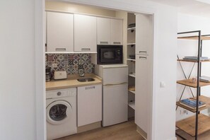 Una kitchenette compacta con lavadora, microondas, tostadora y un refrigerador pequeño.