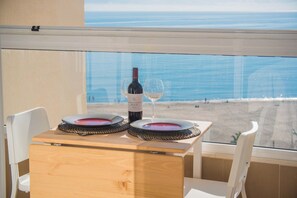 Una mesa con una botella de vino y una copa, frente a una ventana con vista a la playa.