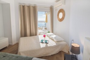 Habitación de hotel con cama, mesita de noche, lámpara y vista al mar.