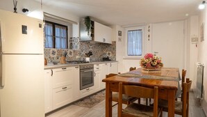 A kitchen with white cabinets, a built-in oven, a dining table with chairs, and a window with curtains. - CASA PINA BED & BREAKFAST (Spoltore)