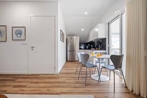 Een moderne keuken met een eethoek, met een houten vloer, witte muren en een groot raam met gordijnen.