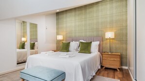 Ein modernes Schlafzimmer mit einem großen Bett, zwei Nachttischen, einer Bank und einem Spiegel.