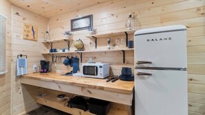 A compact kitchen with wooden walls, a white refrigerator, a microwave, and shelves with various kitchen items. - Seneca Hideaway/Sunken Vessel/Hot Tub (Geneva)