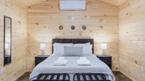 A wooden-paneled bedroom with a bed, two bedside tables, a mirror, and an air conditioning unit. - Seneca Hideaway/Sunken Vessel/Hot Tub (Geneva)