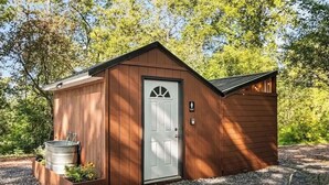 A small wooden shed with a white door, a window, and a small porch area with plants. - Seneca Hideaway/Sunken Vessel/Hot Tub (Geneva)
