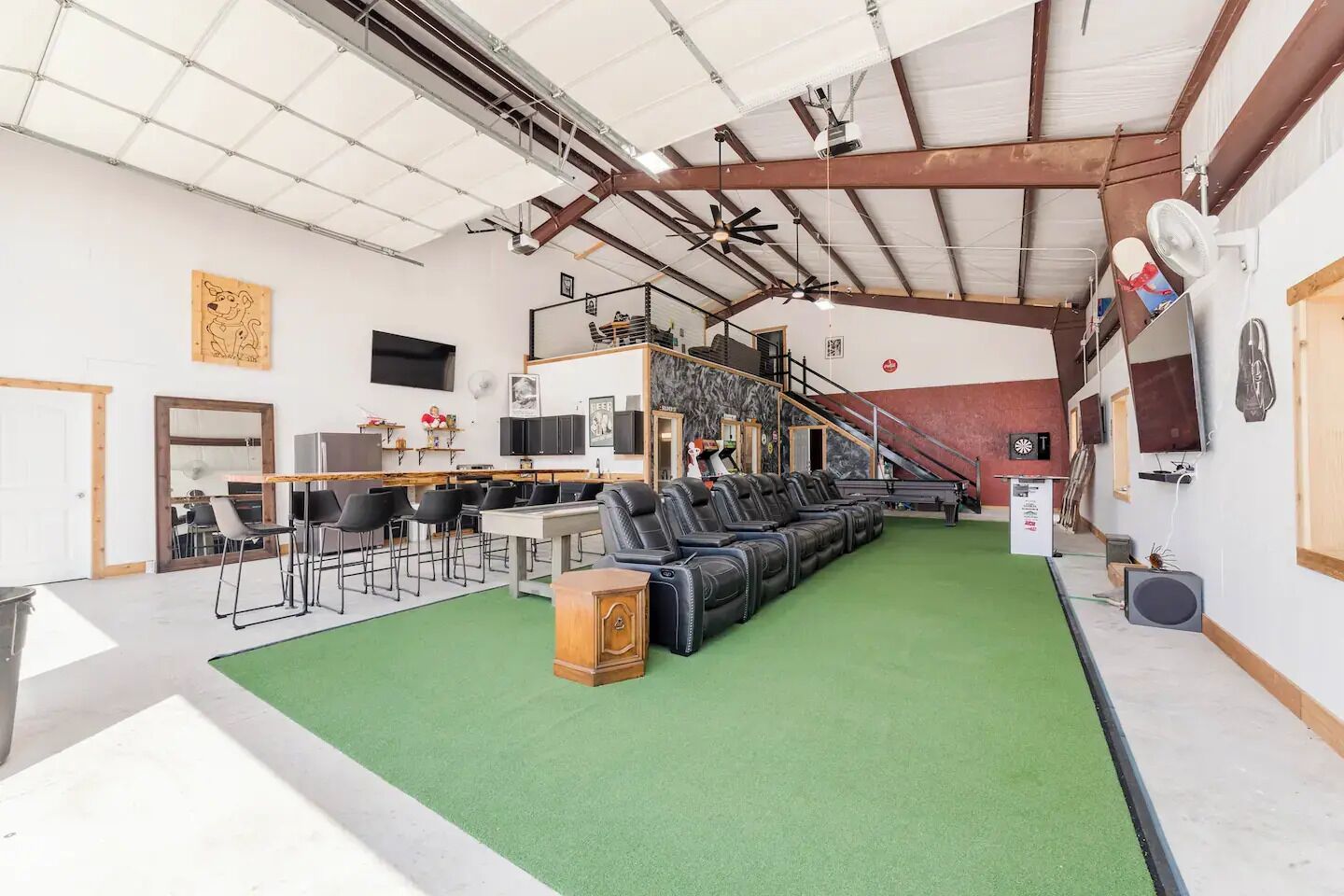Un grand espace intérieur doté d’une moquette verte, de plusieurs canapés en cuir noir, d’un meuble en bois et d’un escalier.