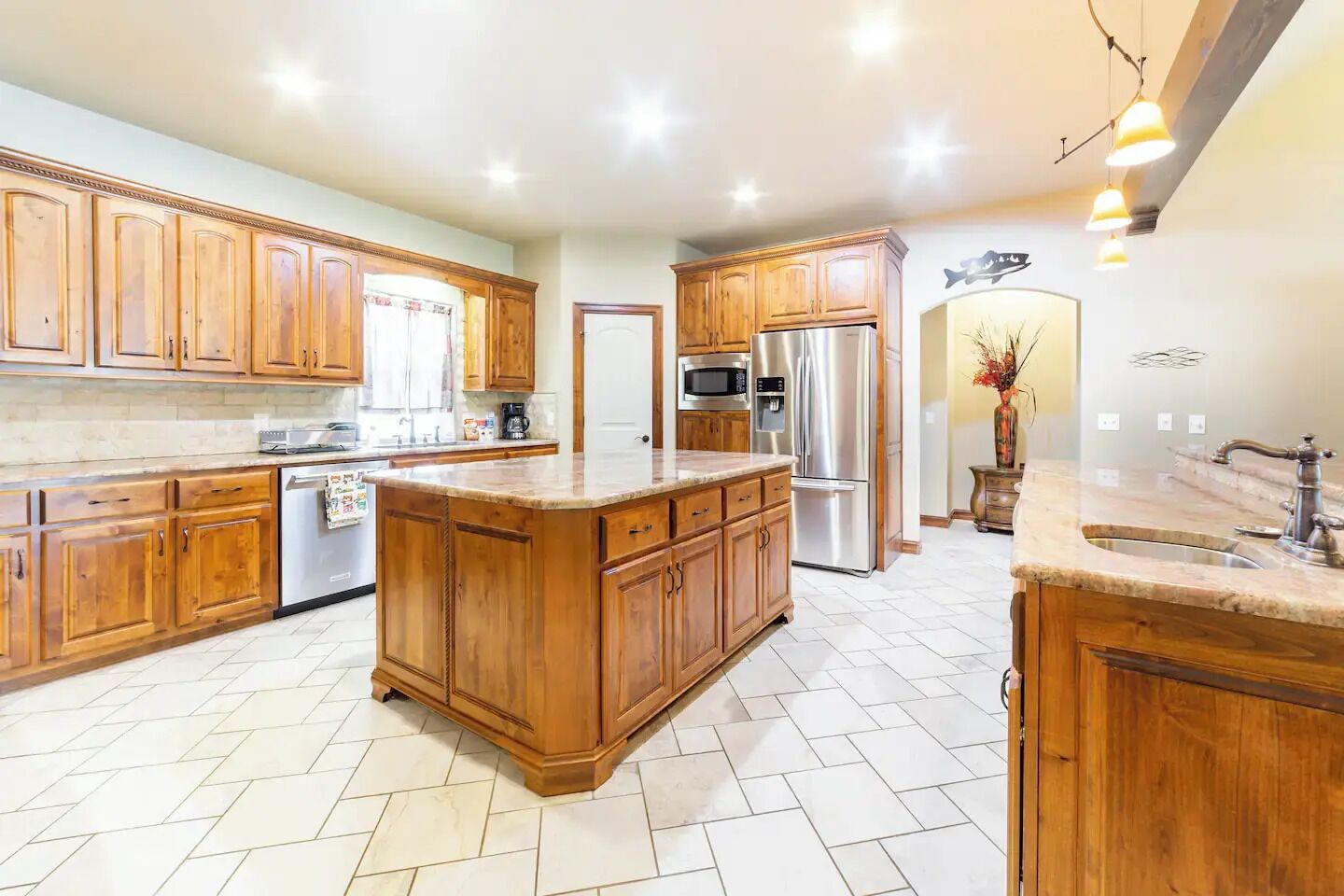 A spacious kitchen with wooden cabinets, a large island, stainless steel appliances, and a tiled floor.