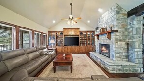 A spacious living room with a stone fireplace, leather sofas, and a large entertainment center.