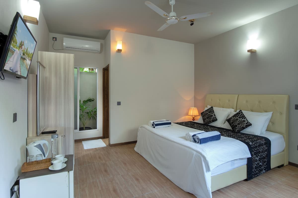 A hotel room with a bed, bedside table, lamp, air conditioning unit, and a television on the wall.