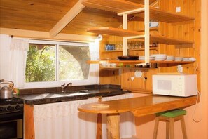 Une cuisine avec des meubles en bois, un four à micro-ondes, une cuisinière et une fenêtre donnant sur un paysage verdoyant.