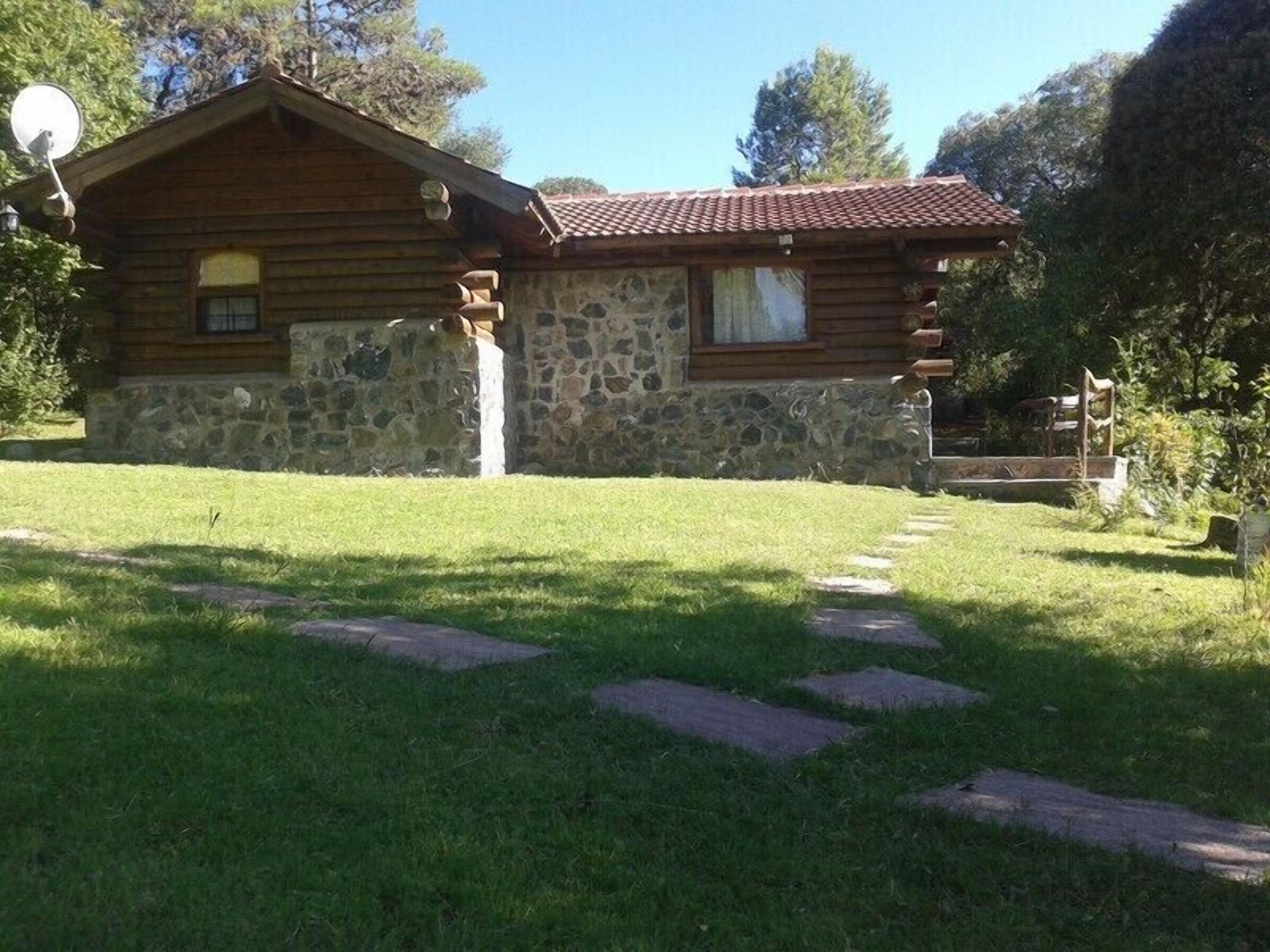 A rustic log cabin with stone walls, a tiled roof, and a stone staircase leading to the entrance.