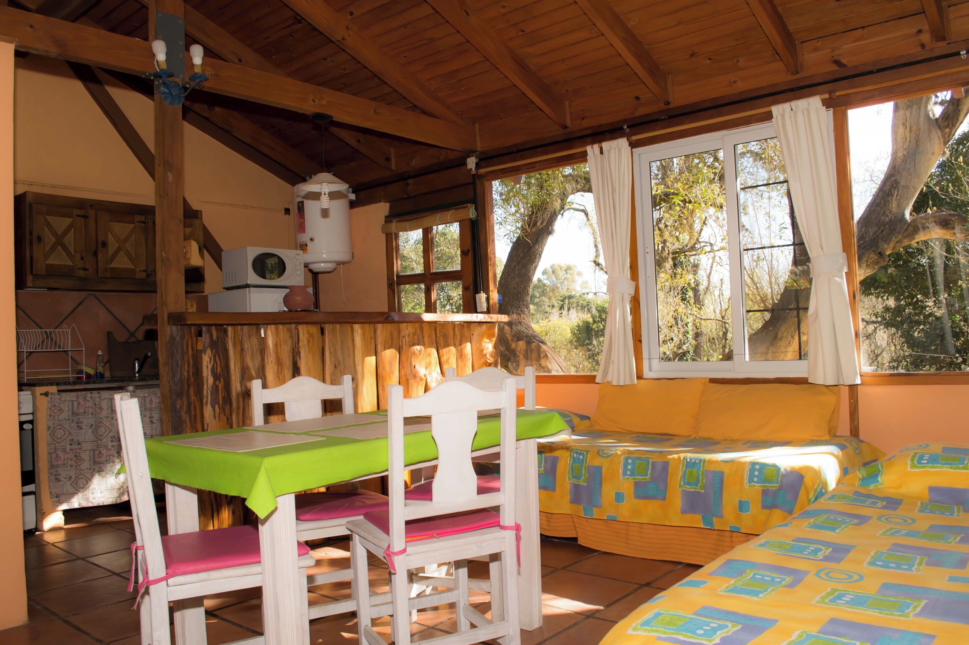 Una habitación acogedora con techo de madera, una mesa de comedor con sillas, una cama con ropa de cama colorida y una ventana con cortinas.