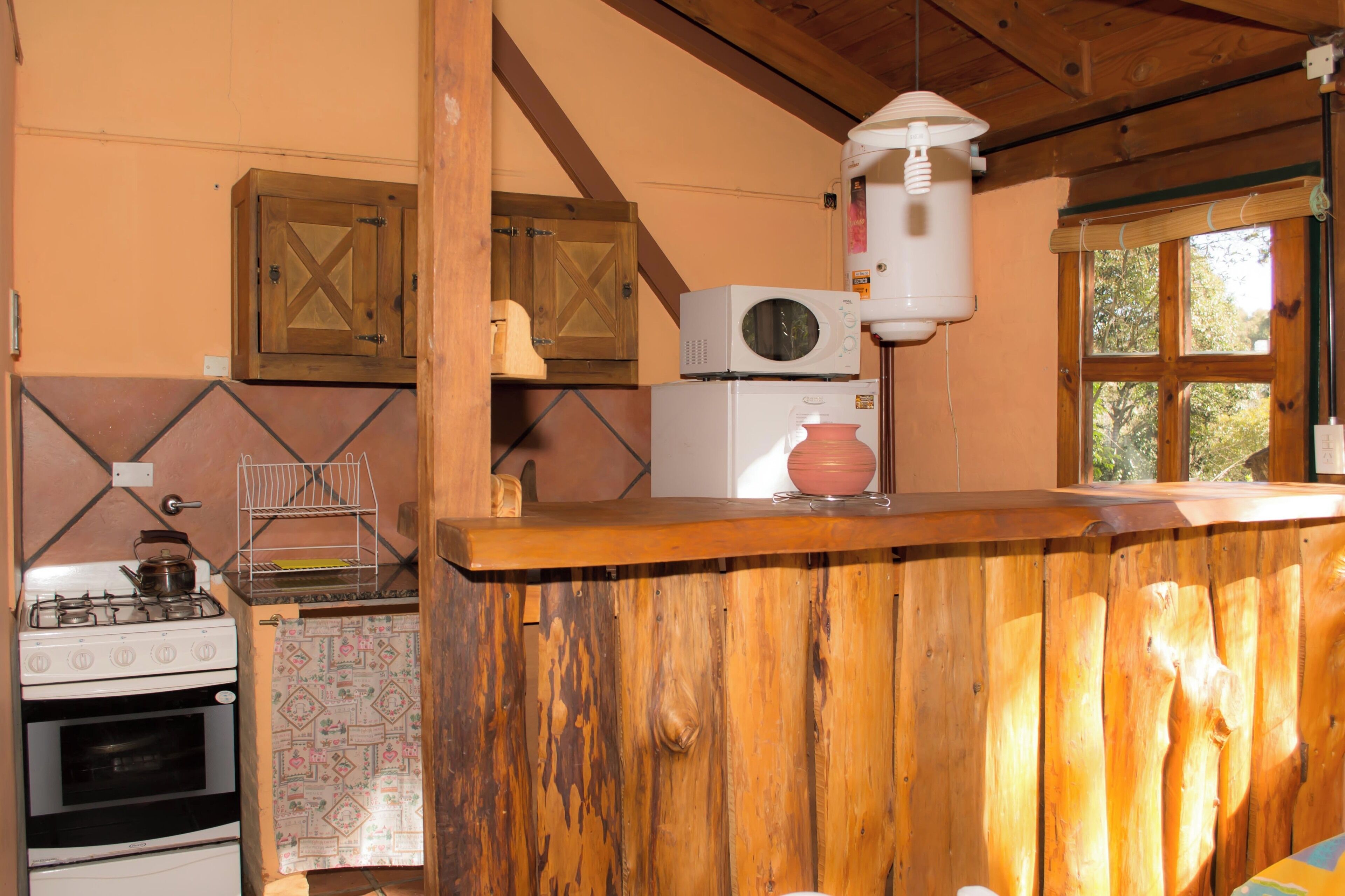 Een keuken met houten kastjes, een fornuis, een magnetron en een hangende lamp.