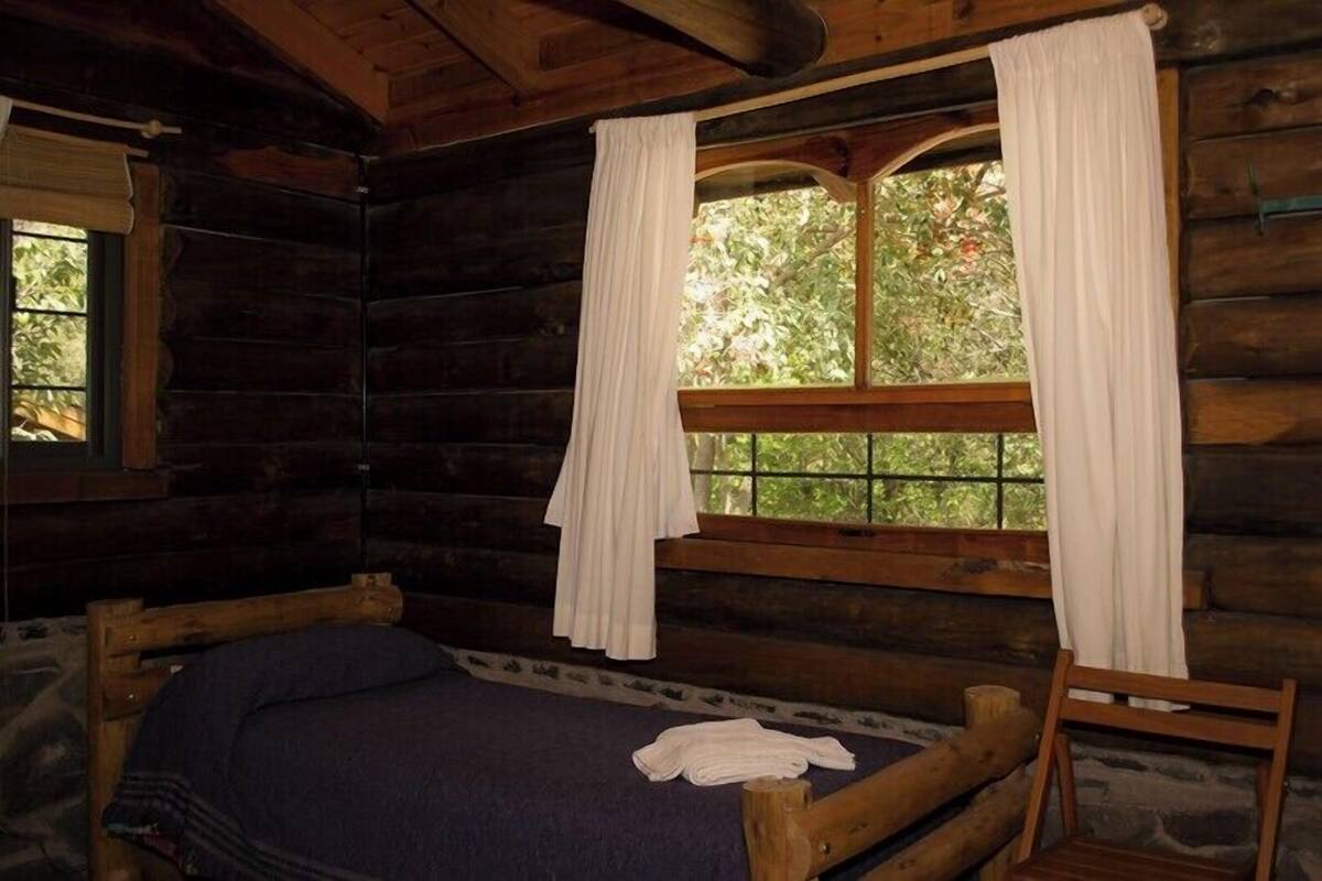 Une chambre de style rustique, avec un lit, une fenêtre avec des rideaux et une vue sur la verdure environnante.