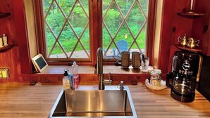 A kitchen with a stainless steel sink, a coffee maker, and a window with a view of greenery.