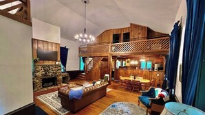 A spacious living area with a stone fireplace, a wooden ceiling, and a dining area with a high wooden ceiling.