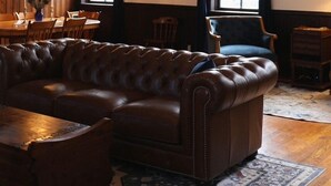 A spacious living room with a large brown leather sofa, a wooden dining table, and a chandelier.